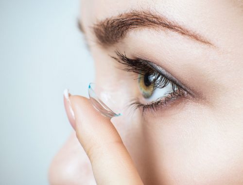 Close-up shot of young woman wearing contact lens for a better view. Over blue background.